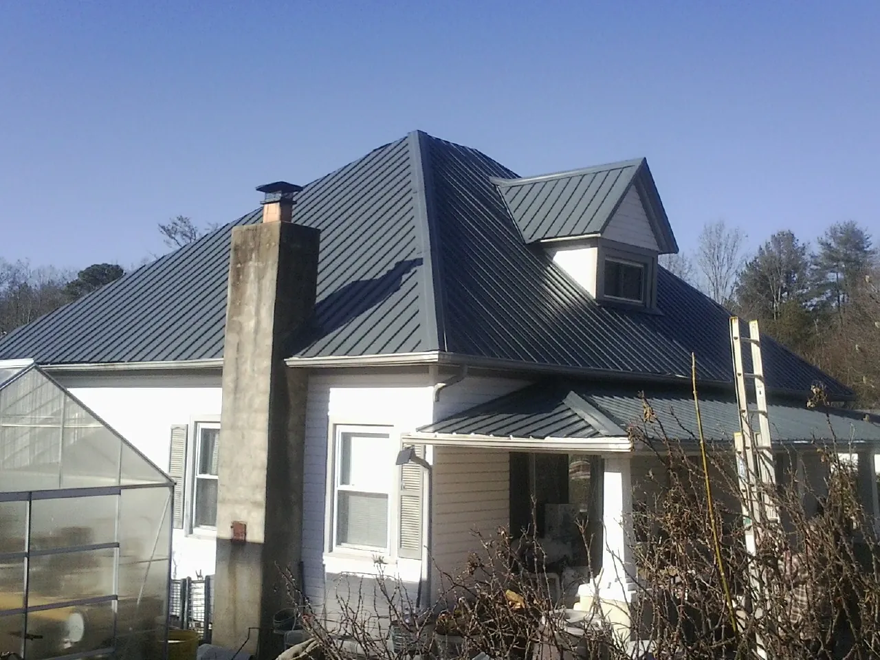 Dark blue standing seam metal roof on a white farmhouse with dormer — Slate & Tile Roof Repair by Roofing Brothers in Camp Pendleton
