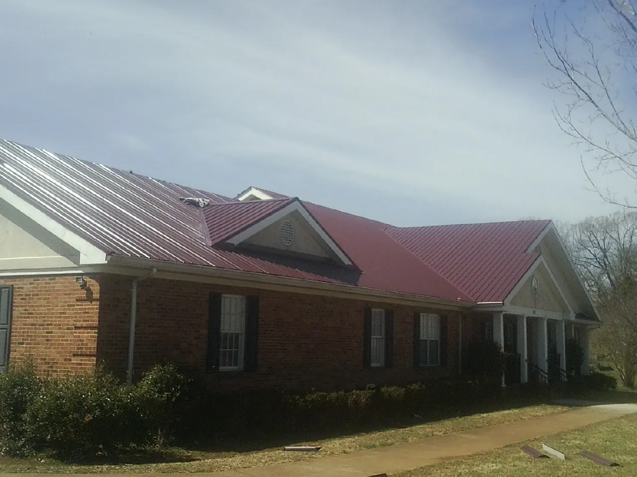 Red metal roof with gabled entries on a long brick building, from a Hail Damage Roof Repair job in Camp Pendleton