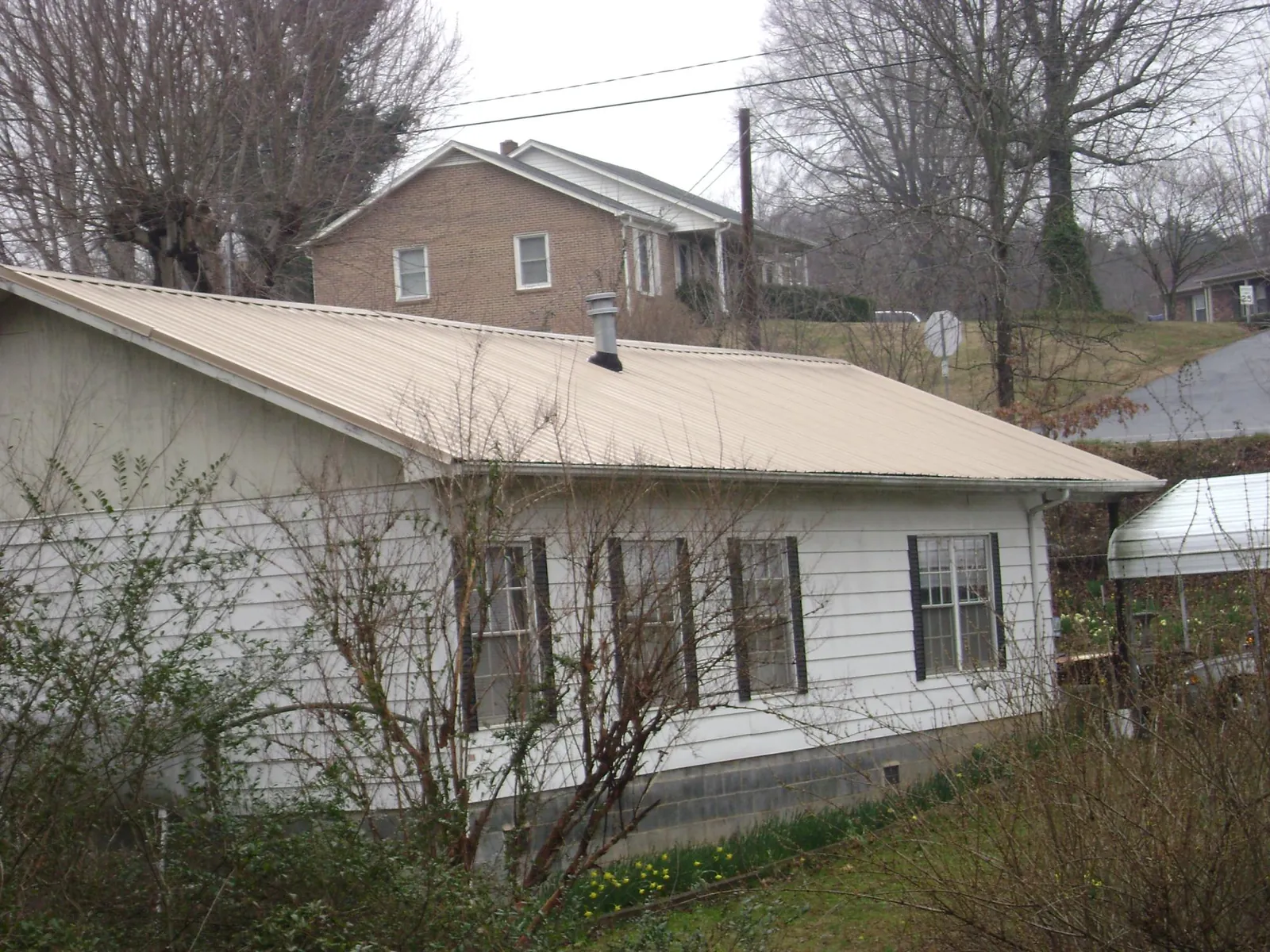 Tan metal roof on a white sided house set into a hillside — Commercial Roofing by Roofing Brothers in Camp Pendleton